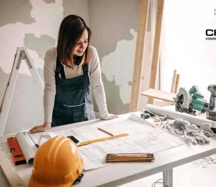 Female contractor reviewing office fitout floor plans during a commercial fitout or renovation project in Perth, with tools, safety helmet and Chest Commercial Projects branding.
