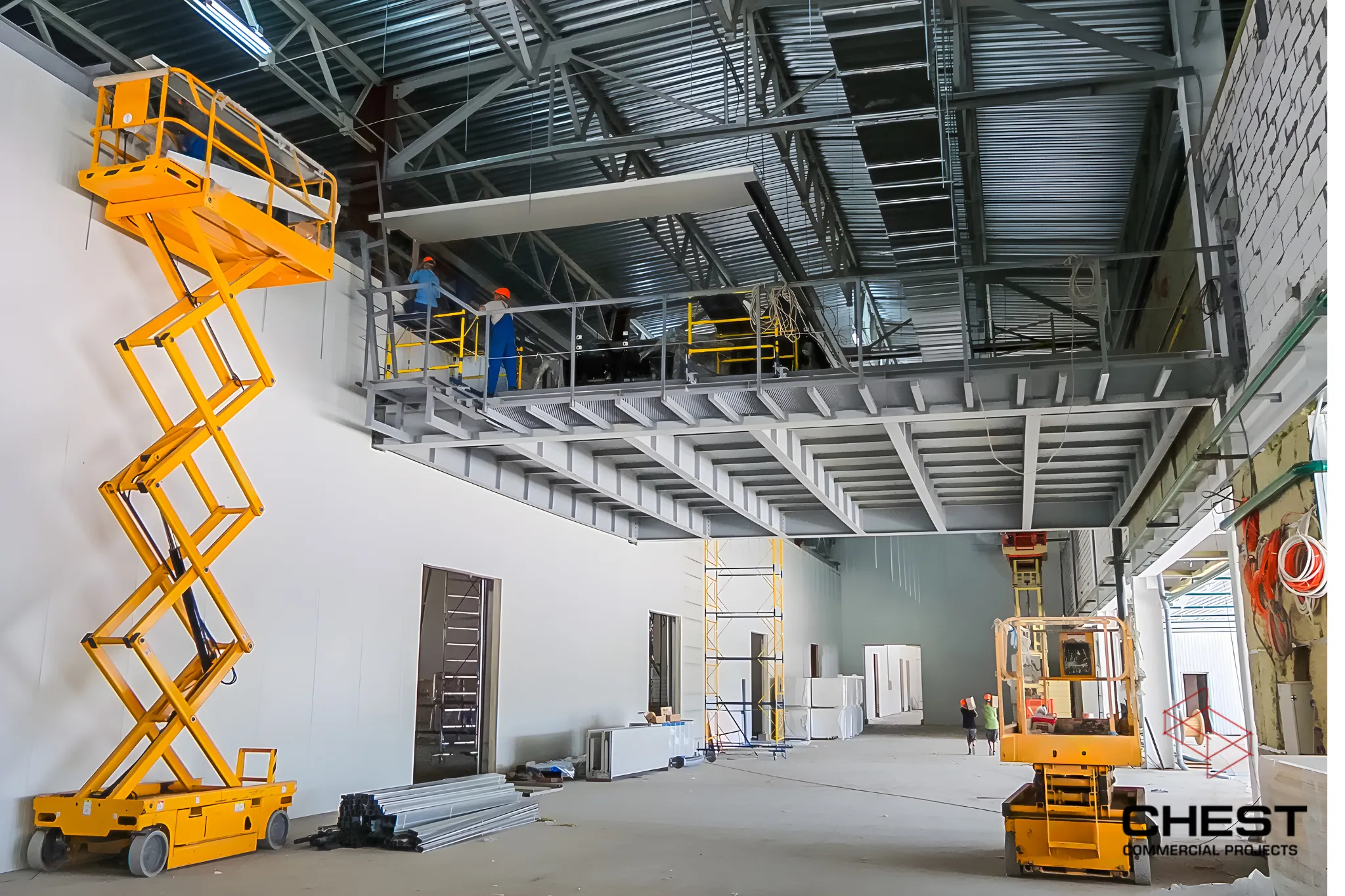 Workers using scissor lifts to construct a steel mezzanine inside a commercial warehouse fitout.