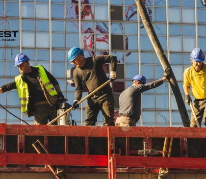 Four construction workers wearing hard hats and safety gear working on a commercial construction site, highlighting workplace safety practices.