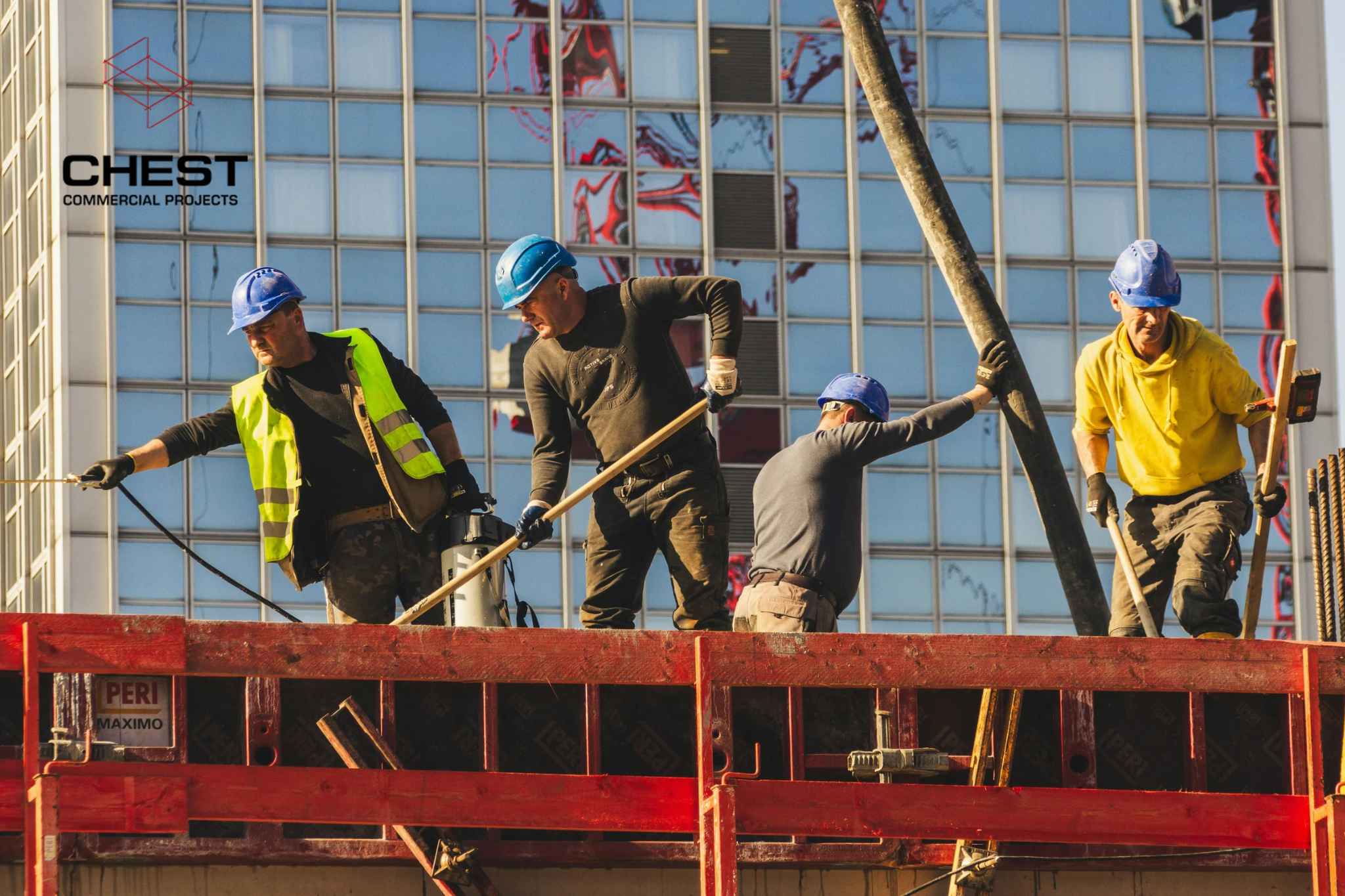 Four construction workers wearing hard hats and safety gear working on a commercial construction site, highlighting workplace safety practices.